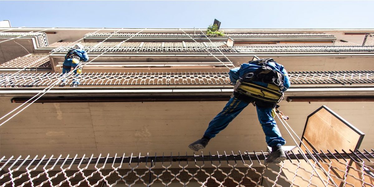 Ouvrier travaillant sous un balcon en ruine, mettant en évidence l'importance de préserver son état pour éviter des détériorations supplémentaires.