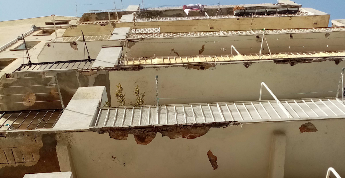 Balcon avec rambarde et ciment qui s'effritent, montrant des signes de détérioration structurelle.
