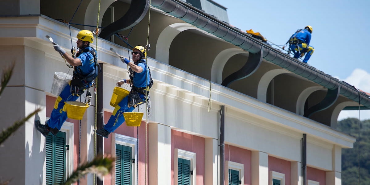 Rénovation de la maison extérieure par des professionnels en toute sécurité, deux ouvriers suspendus sur cordes effectuent les travaux de façade.
