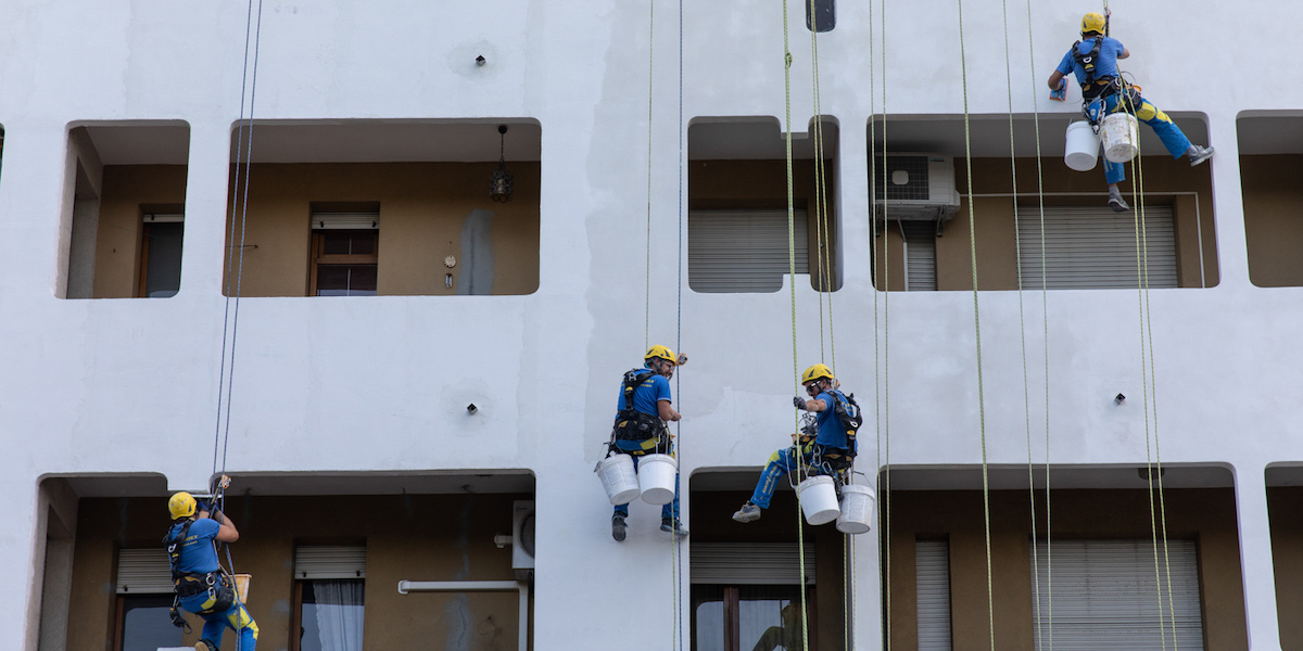 acrobaties de travailleurs sur une corde raide devant la façade d'un bâtiment